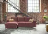 A modern sectional sofa in a loft-style apartment with exposed brick walls and a metal staircase. Produktbild-Vorschau