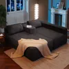 A dark gray sectional sofa with a beige throw blanket draped over it, set in a living room with a fireplace and a tall floor lamp. Produktbild-Vorschau