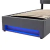 A close-up view of the side of a grey upholstered bed frame with a wooden slat mattress support and blue LED lighting underneath. Náhľad obrázku produktu