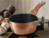 A copper saucepan with a brown handle sits on a black trivet, with beets and garlic in the background. Podgląd zdjęcia produktu