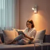 A woman is reading a book on a couch under a wall lamp. Podgląd zdjęcia produktu