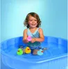 A young girl is playing with rubber ducks in a blue plastic pool. Anteprima dell’immagine prodotto