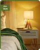 A bedside table with a lamp, book, and blanket next to a bed. Produktbild-Vorschau