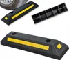 Three black rubber wheel stops with yellow reflective strips and squares are displayed against a white background. One wheel stop is partially under a tire. Produktbild-Vorschau