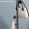 A close-up of a black coat rack with a white handbag and a folded towel hanging on it. A circular detail highlights a hook. Produktbild-Vorschau