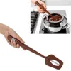 A hand holding a brown digital thermometer spatula over a pot of melting chocolate on a stove. Podgląd zdjęcia produktu