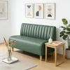 A green sofa is placed in a room with artwork on the wall and a small side table next to it. Produktbild-Vorschau