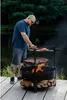 A man is grilling food on a multi-level grill outdoors next to a body of water. Náhled obrázku produktu