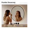 A woman applying makeup in front of a lighted mirror in a bathroom. Produktbild-Vorschau