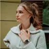 A young woman wearing a light green sweater and a silver digital watch. Produktbild-Vorschau