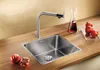 A modern kitchen sink with a faucet, set on a wooden countertop, with pomegranates and a carafe of red liquid nearby. Produktbild-Vorschau