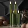 Four green LED candles with 3D flames are arranged in a row, with decorative glitter balls and a jar of pinecones in the foreground and background. Produktbild-Vorschau