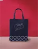 A dark blue tote bag with white embroidery is displayed against a red background and a beige surface. Voir les images du produit