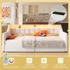 A bedroom scene featuring a white daybed with pink upholstered headboard and cushions. An overhead view of the kitchen area is visible in the background. The bottom of the image displays icons related to lighting features. Voir les images du produit