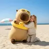 A young girl hugging a large capybara plush toy on a sandy beach. Anteprima dell’immagine prodotto