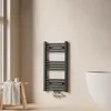 A modern bathroom with a dark anthracite towel radiator mounted on a light beige wall, next to a white bathtub. A wooden stool with a folded towel is placed to the left. Anteprima dell’immagine prodotto