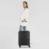 A woman stands holding a black American Tourister suitcase. Produktbild-Vorschau