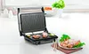 A panini grill with food cooking on it and a plate of cooked food next to it. Produktbild-Vorschau