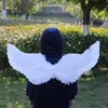 A person wearing a blue hoodie and white angel wings stands in a park. Produktbild-Vorschau