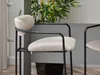 A close-up view of a beige bar stool with a black metal frame, set against a neutral background with a plant in the background. Náhľad obrázku produktu