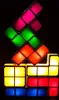 A stack of colorful, illuminated Tetris-like blocks against a black background. Produktbild-Vorschau