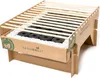 A disposable cardboard grill with charcoal and wooden grates, set against a white background. Produktbild-Vorschau