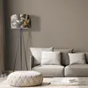 A floor lamp with a floral shade stands next to a sofa with cushions and a tufted ottoman in a room. Produktbild-Vorschau