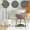 A wax burner with a ceramic bowl on a metal stand, next to a white cup. Produktbild-Vorschau