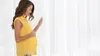 A pregnant woman is standing by a window, touching her belly. Produktbild-Vorschau