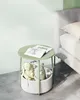 A round green side table with a storage basket underneath holding stuffed toys, next to a bed. Náhled obrázku produktu