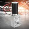 A geared DC motor is shown in the foreground against a blurred background of a modern building interior with sunlight streaming in. Podgląd zdjęcia produktu