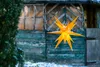 A yellow star-shaped decoration hangs in front of a weathered green wooden shed with a window. Produktbild-Vorschau