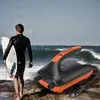 A surfer holding a surfboard on a beach with an electric air pump in the foreground. Produktbild-Vorschau