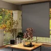 A balcony or patio with a grey roller blind, a wooden table with a pitcher and glasses, and potted plants. Produktbild-Vorschau