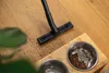 A vacuum cleaner head is shown cleaning up spilled coffee grounds from a wooden floor near a pet bowl. Náhled obrázku produktu