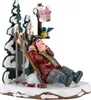 A figurine of a person relaxing in the snow with skis and a signpost. Produktbild-Vorschau