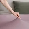 A hand is shown pressing down on a purple fabric, likely a bedsheet, with pillows in the background. Podgląd zdjęcia produktu