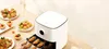 An air fryer is shown on a table with various prepared foods, including chicken wings, small tarts, and meatballs. Podgląd zdjęcia produktu