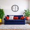 A living room scene with a blue sofa, decorative pillows, plants, and a wall clock. Voir les images du produit