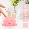 A pink pig-shaped LED night light is shown on a white desk with a vase of flowers and pencils in the background. Hands are pointing at the light, indicating interaction. Podgląd zdjęcia produktu