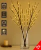 Two LED decorative branches with warm white lights in a glass vase, placed on a table with a candle. Produktbild-Vorschau