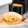 A black air fryer with a basket full of french fries is shown next to a brown paper liner filled with french fries. Podgląd zdjęcia produktu