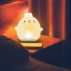 A cute, glowing bunny-shaped night light sits on a bedside table next to a bed. Produktbild-Vorschau