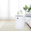 A white air purifier is placed on a rug next to a sofa in a bright room with sheer curtains. Produktbild-Vorschau