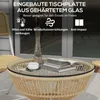 A round rattan coffee table with a glass top, set on a patio with a chair and books on the table. Produktbild-Vorschau