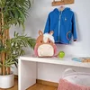 A child's horse-themed backpack and a blue jacket are displayed on a white shelf, with a potted plant to the left. Anteprima dell’immagine prodotto