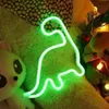 A neon dinosaur light is displayed on a fluffy surface, surrounded by stuffed animals and Christmas decorations. Podgląd zdjęcia produktu