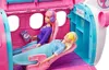 Two Barbie dolls are inside a pink and blue toy airplane. One doll is sitting up and wearing headphones, holding a small booklet. The other doll is lying down with a yellow eye mask on. Produktbild-Vorschau