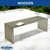 A modern metal bench with a book on it, placed on a white outdoor patio with greenery in the background. Produktbild-Vorschau