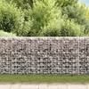 A gabion wall filled with stones, with green bushes in the background and a paved area in the foreground. Produktbild-Vorschau